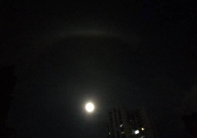 今天晚上的月亮旁边围绕着半圈彩色的光,一个人站在台阶上望着它,是美
