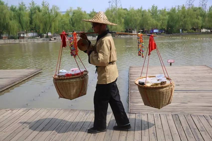 挑夫敲着铜锣,挑着扁担,扁担两头的竹筐里装着各种各样的精美小吃,有